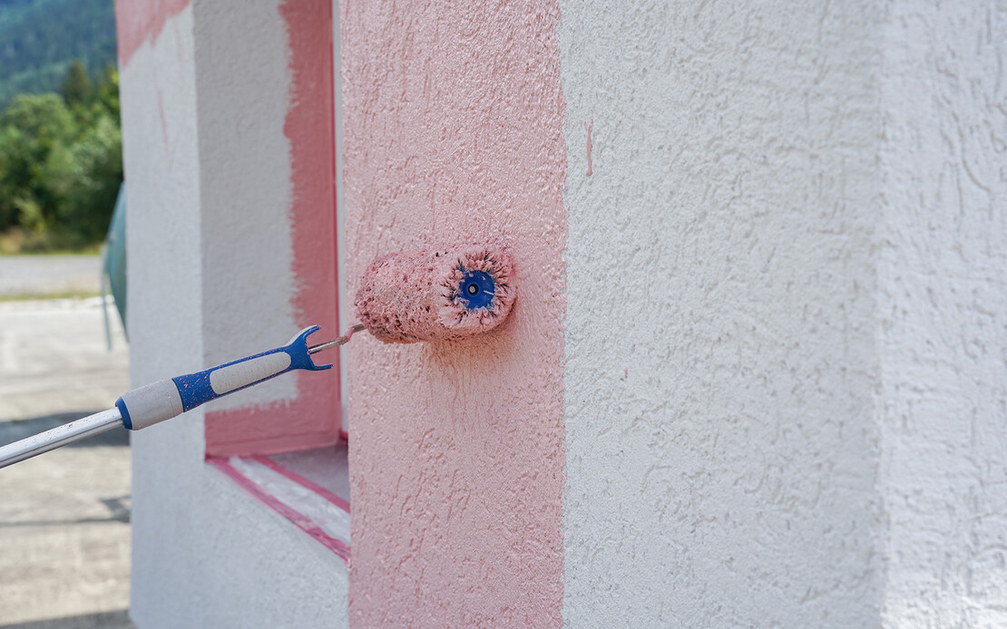 Eine wei&szlig;e Wand wird mit einer gro&szlig;en Farbrolle rosa gestrichen.
