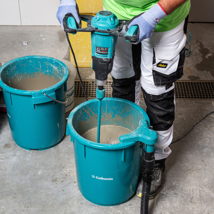 Personne mélange soigneusement la masse d'égalisation dans le seau à l'aide d'un mélangeur électrique Collomix.