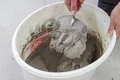 Person rührt Zementmörtel in einem Eimer für Heimwerkerprojekt an.