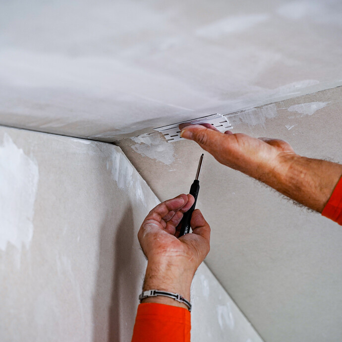 La surface de la construction sèche est marquée avec un morceau de profilé de joint de dilatation et un crayon.