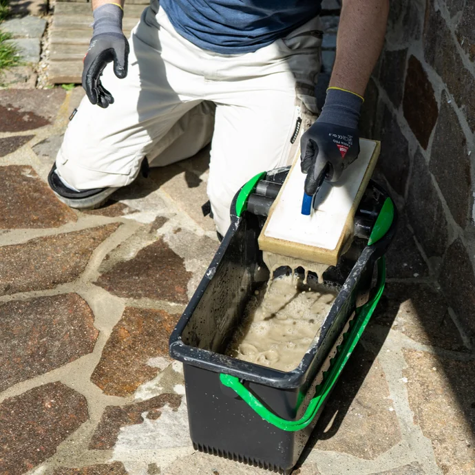 Un bricoleur mélange le Mortier dans un seau pour enduire des murs de jardin ; il porte des gants pour une application sûre et propre.
