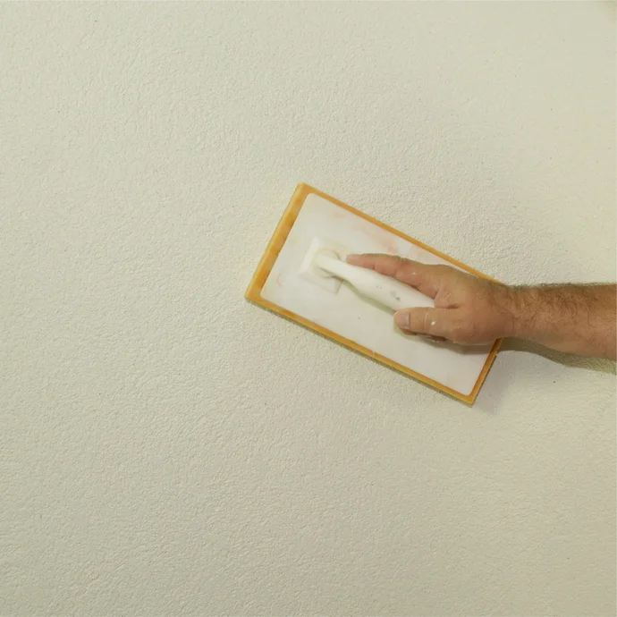 Hand glättet Putz auf einer weißen Wandoberfläche mit einer Schwammscheibe. Ideal für gleichmäßige, glatte Ergebnisse.