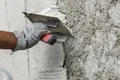 Hand trägt Putz mit Kelle auf Außenwand auf, Baumit DIY-Projekt für Heimwerker.