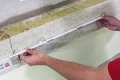 Messen einer Wandfläche mit einem Maßband zur Vorbereitung von Dämmarbeiten.