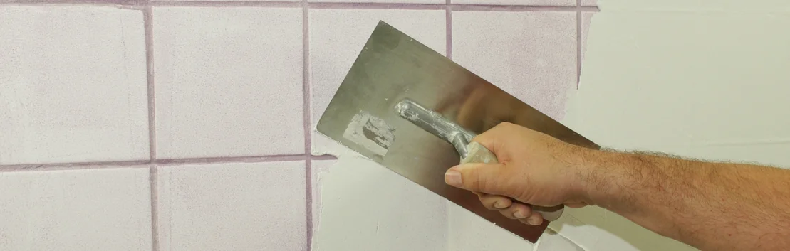 Un bricoleur utilise une truelle pour jointoyer les carreaux dans le cadre d&rsquo;un projet de salle de bains.