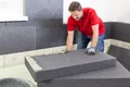 Un bricoleur pose des panneaux isolants à l’intérieur à l’aide de matériaux Baumit pour une isolation thermique efficace.