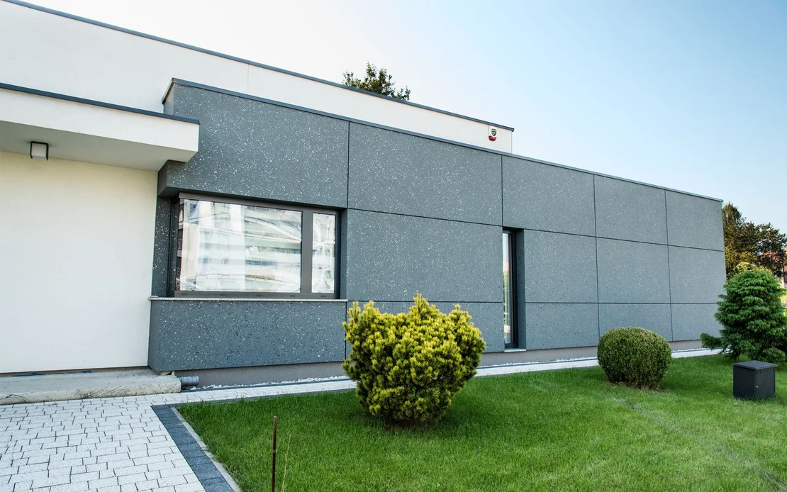 Moderne Fassade mit grauen Platten, umgeben von gepflegtem Garten, ideal f&uuml;r kreative Heimwerkerprojekte.