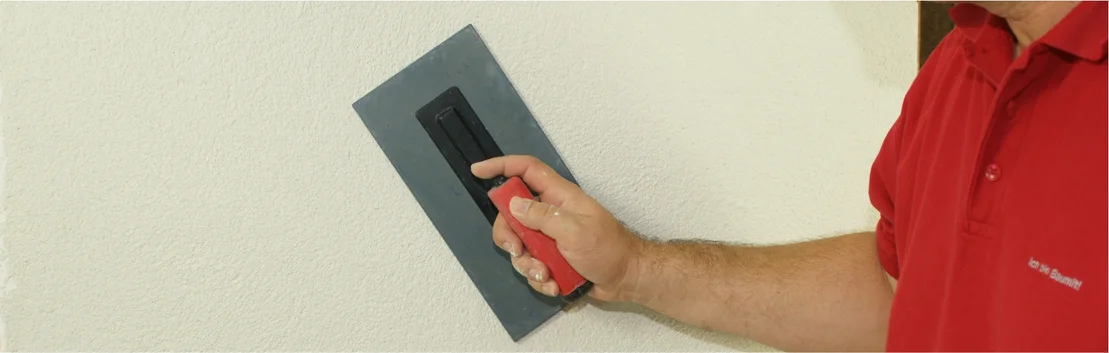Heimwerker tr&auml;gt mit Gl&auml;ttekelle Putz auf eine Wand auf.