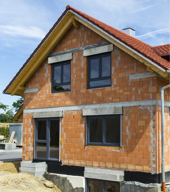 Maison en gros œuvre avec une façade en briques non crépie, prête pour les travaux d’enduit et d’isolation avec les produits Baumit en vue de sa finalisation.