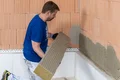 Mann trägt Dämmstoffplatte auf Mauerwerk auf, Schritt zur Wärmedämmung von Innenwänden, DIY-Anleitung für Heimwerker.