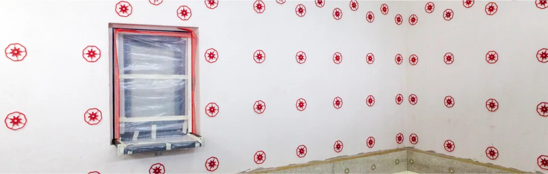 Innenwand mit Dämmstoffbefestigungen, Fensterrahmen abgeklebt; Schritt für Schritt zum effizienten Dämmen und Gestalten von Wänden.