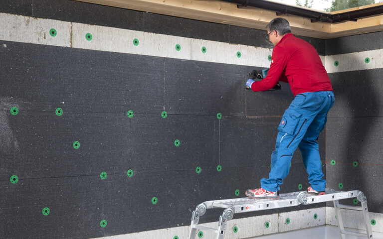 Heimwerker bohrt Löcher, um die EPS-Dämmplatten an der Fassade mit dem Thermotop Schlagdübel H2 plus zu befestigen.
