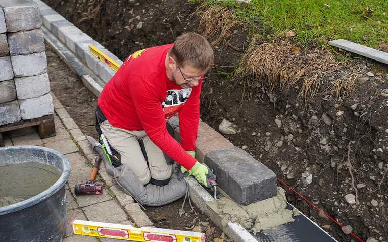 Mit einer Kelle wird überschüssiger Mörtel nach dem Setzen der Steine entfernt.