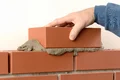 Un bricoleur construit un mur en briques avec du Mortier ; sa main ajoute une brique supplémentaire en haut pour assurer la solidité de la construction.