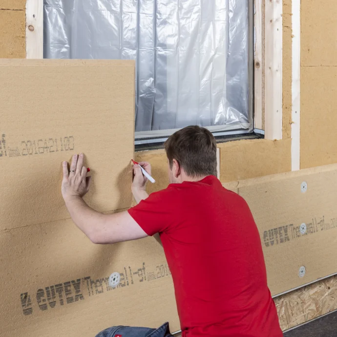 Mann montiert Dämmplatten an Außenwand; Schritt-für-Schritt-Anleitung zur Fassadendämmung für Heimwerker.