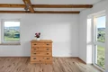 Helles Wohnzimmer mit Holzbalkendecke, Holzboden und einer Kommode, ländlicher Ausblick durch große Fenster.