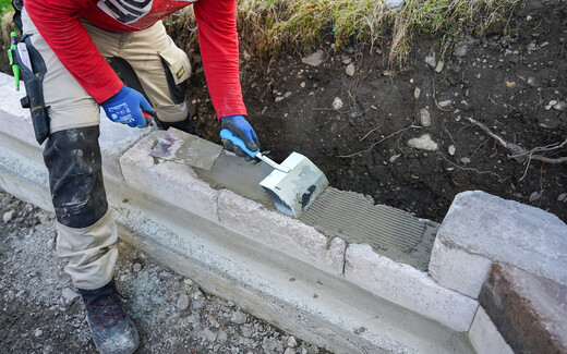 Natursteine und Betonsteine kleben mit Baumit Steinkleber Trass - Mit einer Klebekelle wird der aufgetragene Steinkleber aufgeraut, um eine bessere Haftung zu gewährleisten. So kann der nächste Mauerstein der Gartenmauer gesetzt werden.