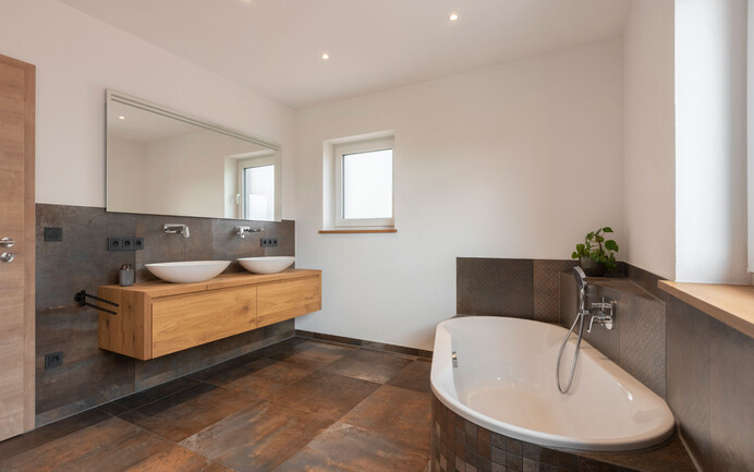 Design moderne d'une salle de bains avec différents panneaux sombres de couleur rouille parfaitement mis en scène avec les murs blancs brillants à la structure finement feutrée avec l'enduit noble Baumit InStyle Edelweiss.