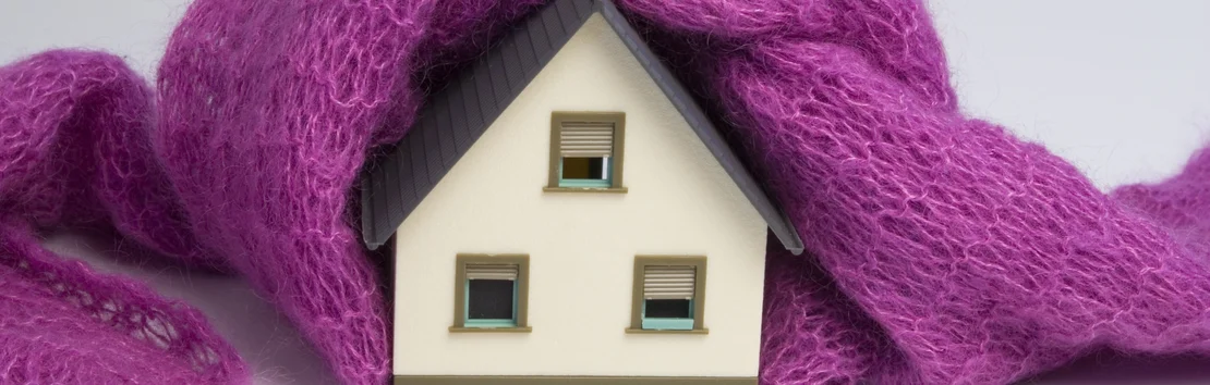 Une maison miniature envelopp&eacute;e dans une couverture violette aux tons chauds, symbolisant l&rsquo;isolation des b&acirc;timents et la protection des projets de bricolage.