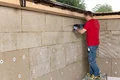 Heimwerker befestigt Dämmplatten an der Außenwand eines Hauses.