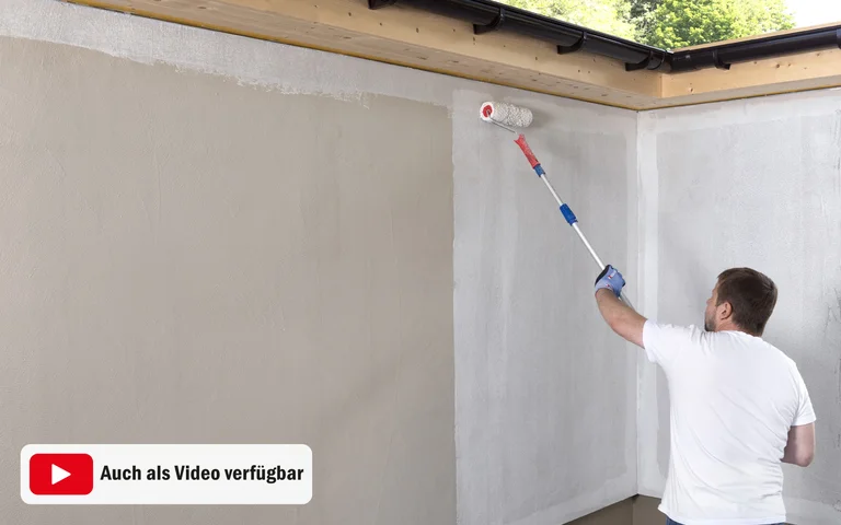 Heimwerker streicht Innenwand mit Farbrolle; Schritt-für-Schritt-Anleitung für DIY-Renovierung auf Baumit-Website verfügbar.