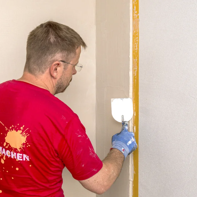 Mann verspachtelt Wand mit Glättekelle bei Sanierungsprojekt; Schritt-für-Schritt-Anleitung für Heimwerker.