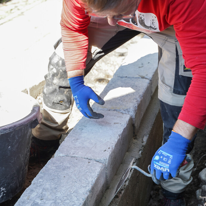 Eine Person zieht mit einer Kelle den Gefälle- und Betonspachtel entlang der Mauerkante auf, um die Hohlkehle zu erstellen.