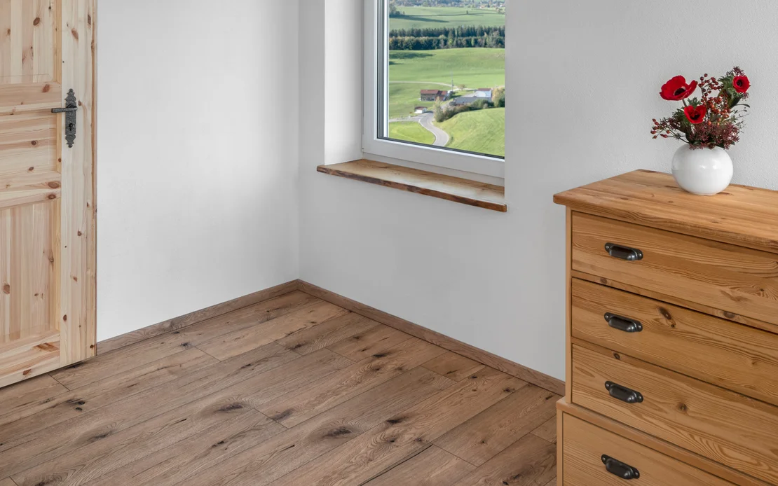 Helles Wohnzimmer mit Holzfu&szlig;boden, Fenstersitzbank und Holzkommode, ideal f&uuml;r Renovierungsprojekte mit Baumit-Produkten.