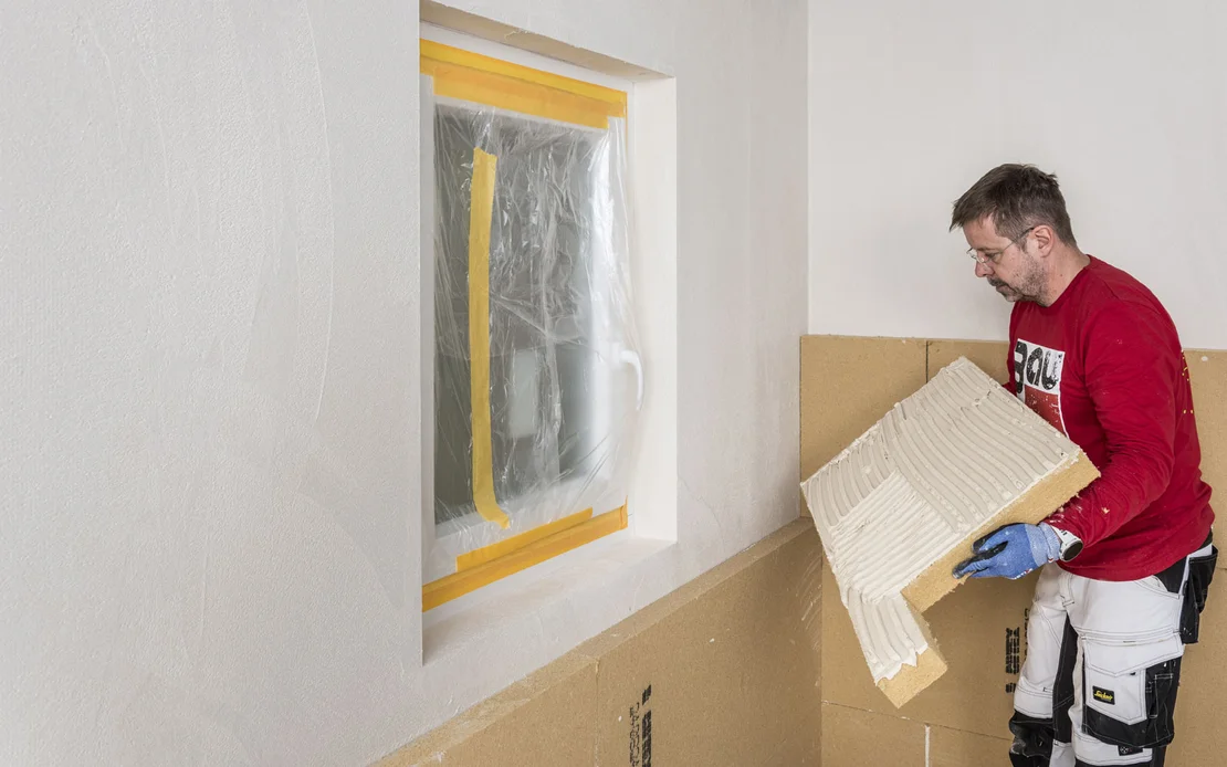 Heimwerker klebt Holzfaserdämmplatte an die Wand. Die Dämmplatte ist in L-Form zugeschnitten. Baumit Selbermachen DIY-Anleitung.