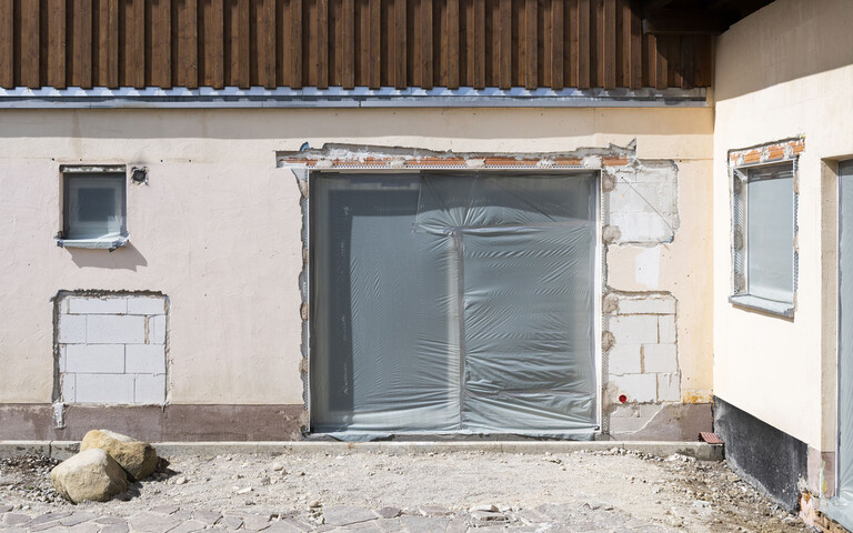 Zeit für eine Sanierung: Alte Hausfassade, die saniert werden muss, mit abgeschlagenem Putz, kleinem Fenster und großer Terrassentüre.