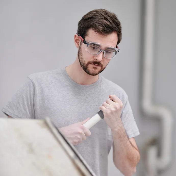 Mann verwendet Spachtelmasse mit Werkzeug, trägt Schutzbrille, ideal für Heimwerker bei Renovierungsarbeiten.