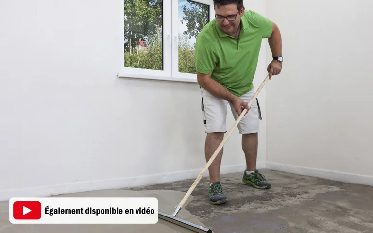 Un homme nivelle le sol d’une pièce à l’aide d’une taloche de lissage afin d’obtenir une surface régulière dans le cadre d’une rénovation en bricolage.