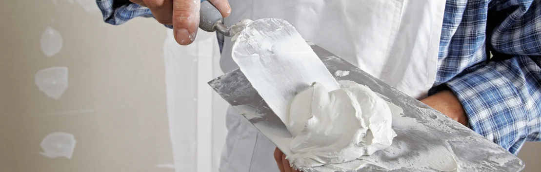 Un bricoleur applique du mastic &agrave; l'aide d'une truelle, id&eacute;al pour les projets de r&eacute;novation DIY.