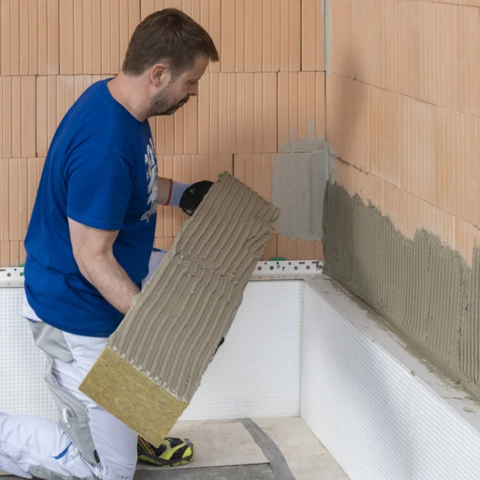 Un bricoleur pose un panneau isolant sur un mur ; une étape pour améliorer l’isolation thermique avec les produits Baumit.