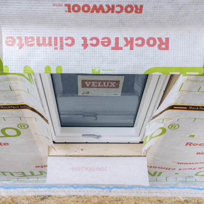 Pose d’un isolant sur une fenêtre de toit avec un film de protection pour une isolation optimale et une protection contre les intempéries dans le cadre d’un projet de bricolage.