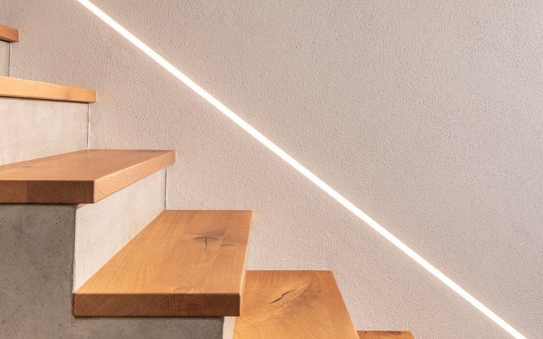 Modernes Treppenhaus mit Beton, indirekter Beleuchtung und dem wohngesunden Baumit Edelputz InStyle Edelwei&szlig;.
