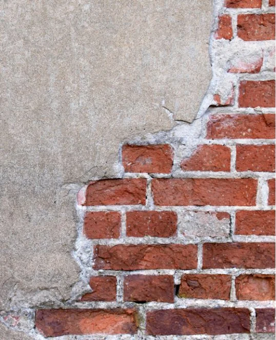Mur en briques dont l’enduit est partiellement effrité, adapté à une instruction de rénovation et de réhabilitation des façades.