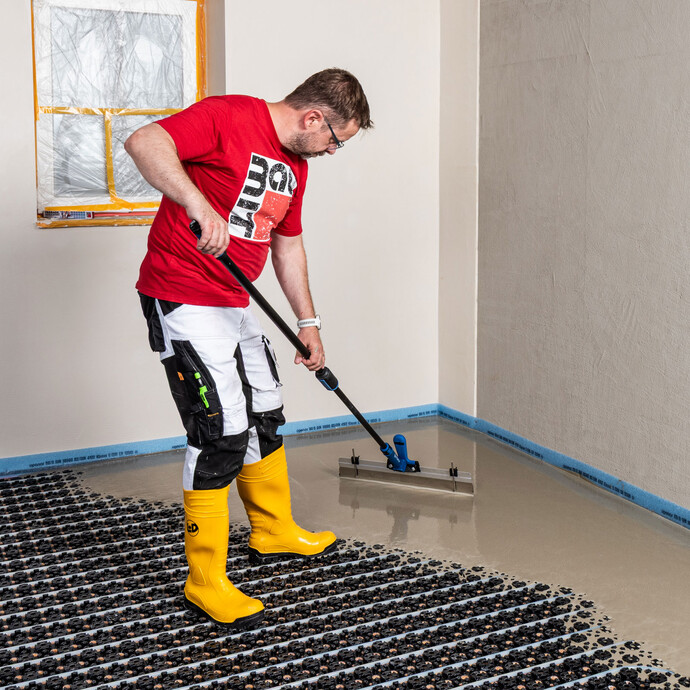 Le bricoleur étale la masse d'égalisation autonivelante à l'aide d'une raclette.