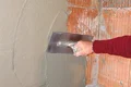 Eine Person glättet frischen Putz mit einer Kelle auf einer Backsteinwand.