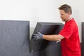 Un homme en t-shirt rouge pose des panneaux isolants sur un mur. Instruction à faire soi-même sur Baumit destinée aux bricoleurs.