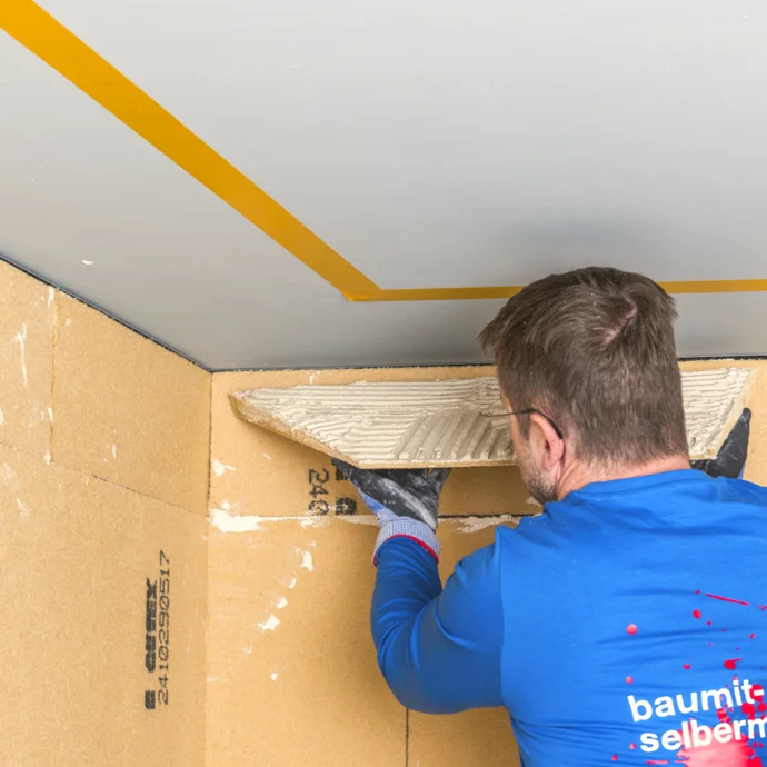 Heimwerker verputzt Kartonwand mit Spachtelmasse; Schritt zur Wandrenovierung mit Baumit-Produkten.