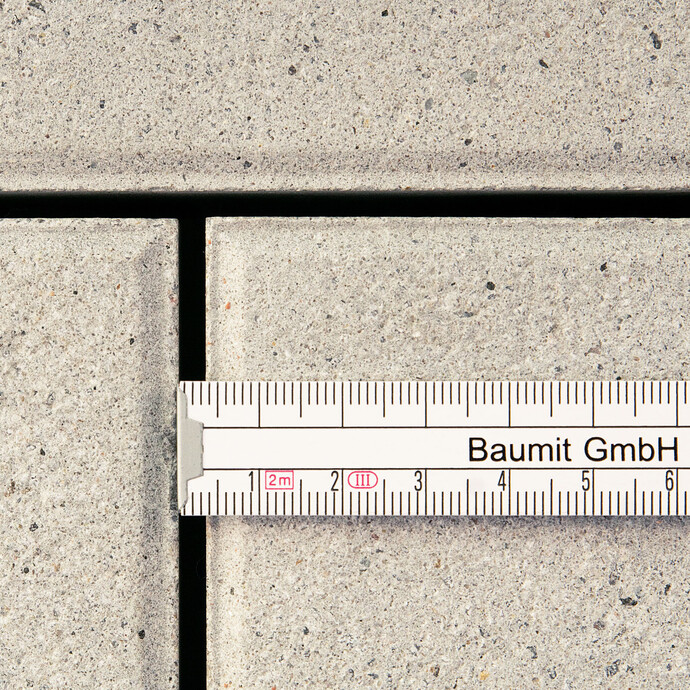 Bevor die Betonsteinplatten mit dem Pflasterfugenmörtel Fix verfugt werden, wird die Mindestfugenbreite mit einem Lineal überprüft.