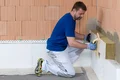 Heimwerker dämmt eine Hauswand mit Isolierplatten und Mörtel, Baumit Anleitung für effektive Wärmedämmung.