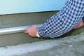 Heimwerker zieht Putzschicht mit Richtlatte auf Fassade glatt.