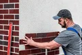 Un bricoleur pose des pierres de parement sur la façade d’une maison ; instructions étape par étape pour un projet de construction.