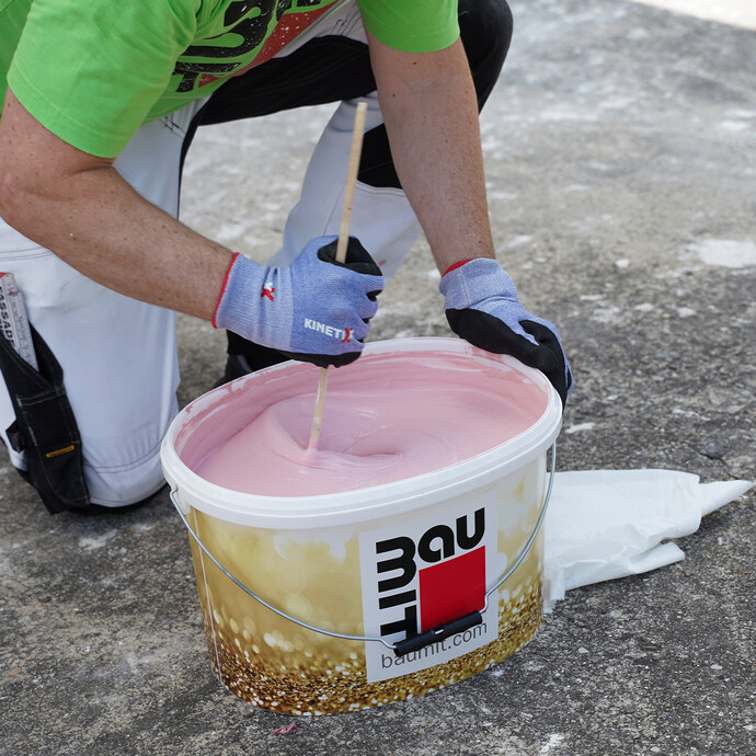 Die rosa Fassadenfarbe wird im Baumit Eimer mit einem Rührstock aufgerührt.