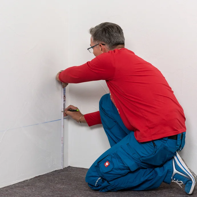 Handwerker zeichnet die zweite Bohrlochreihe 5 cm über der ersten Bohrlochreihe an.