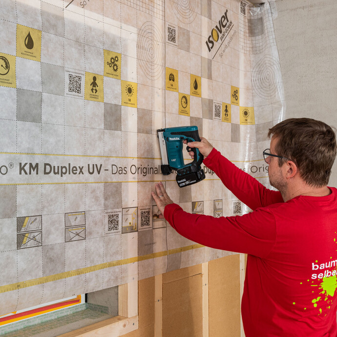 Baumit Handwerker überspannt das Fenster mit der Dampfbremse ISOVER KM Duplex UV und tackert sie an der Tragkonstruktion der ersten Dämmebene der Innendämmung fest. Anleitung zum Selbermachen.