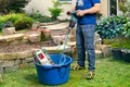 Heimwerker mischt Baummörtel im Garten mit einem Rührgerät in einem blauen Eimer.