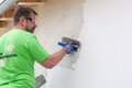 Le bricoleur applique l'enduit fouetté de Munich sur la façade à l'aide d'une truelle.